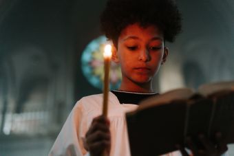 A young boy in a church holding a candle and reading a Bible, conveying concentration and spirituality.
